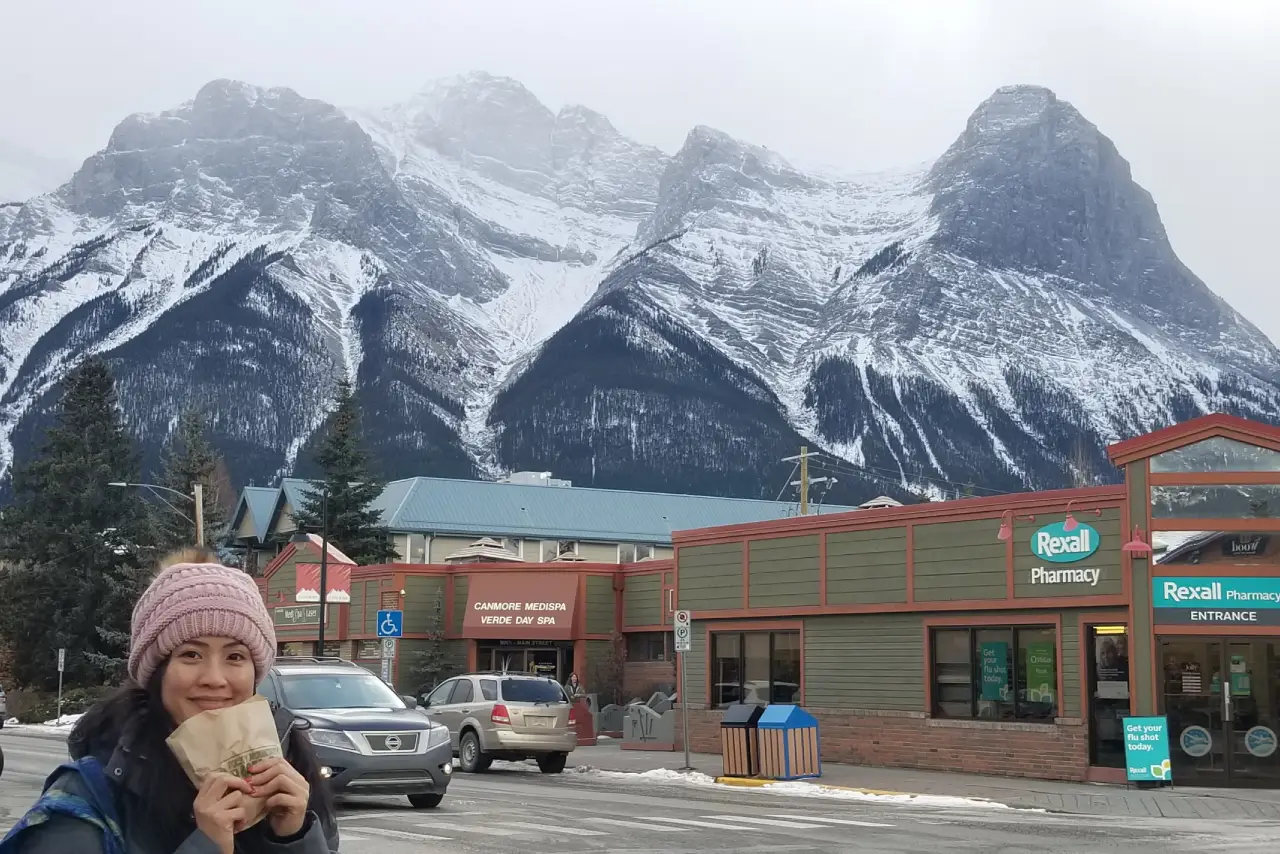 Snow-covered mountains behind a street with shops and cars.