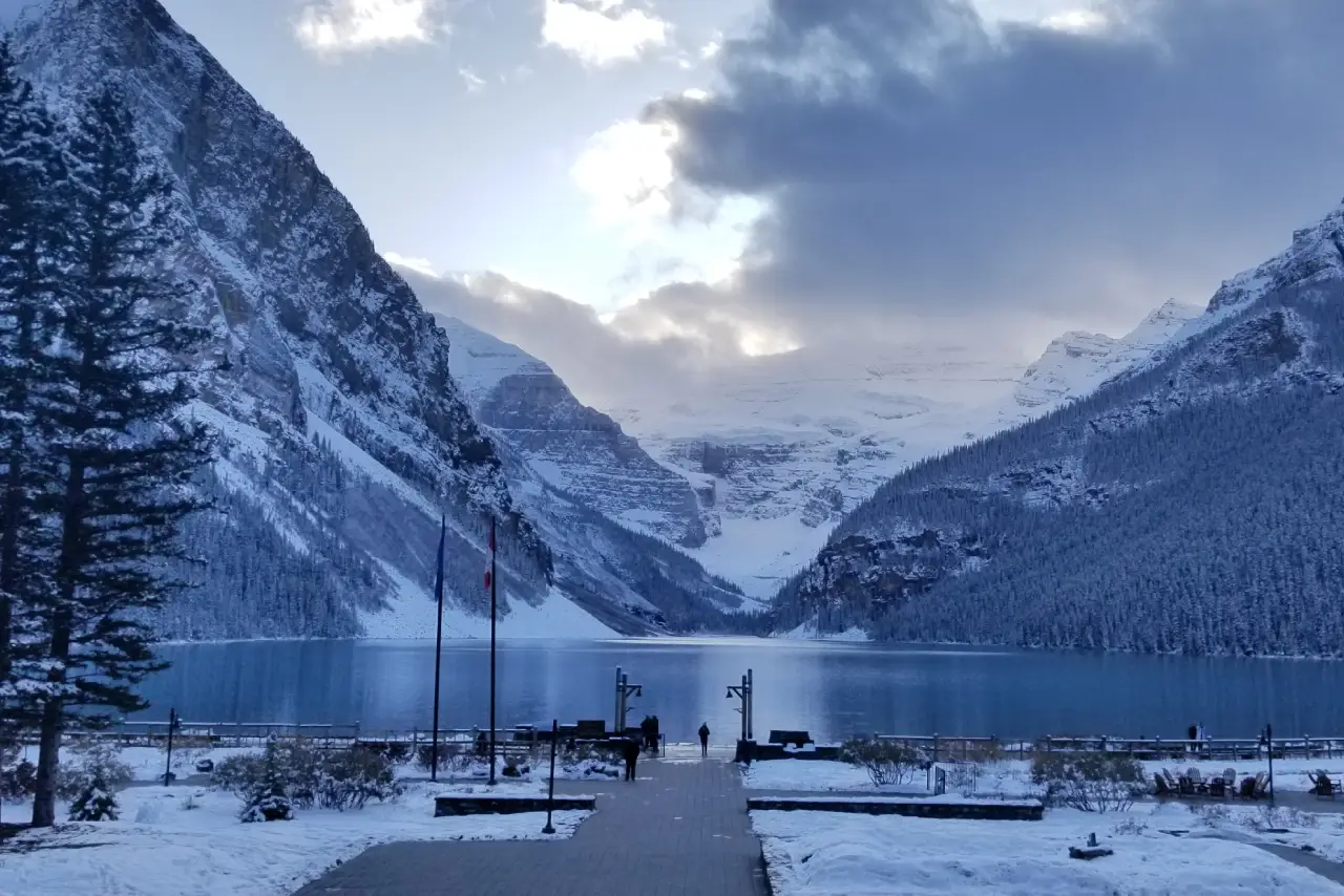 A snowy lakeside walkway leading to a mountain range at dusk.